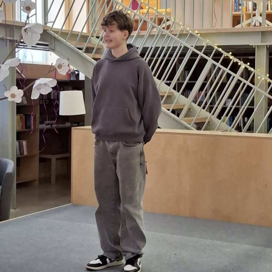 Uz skatuves,Eliass Jānis Priedīts skaita dzejoli Fonā ir grāmatu plaukti un metāla kāpnes.