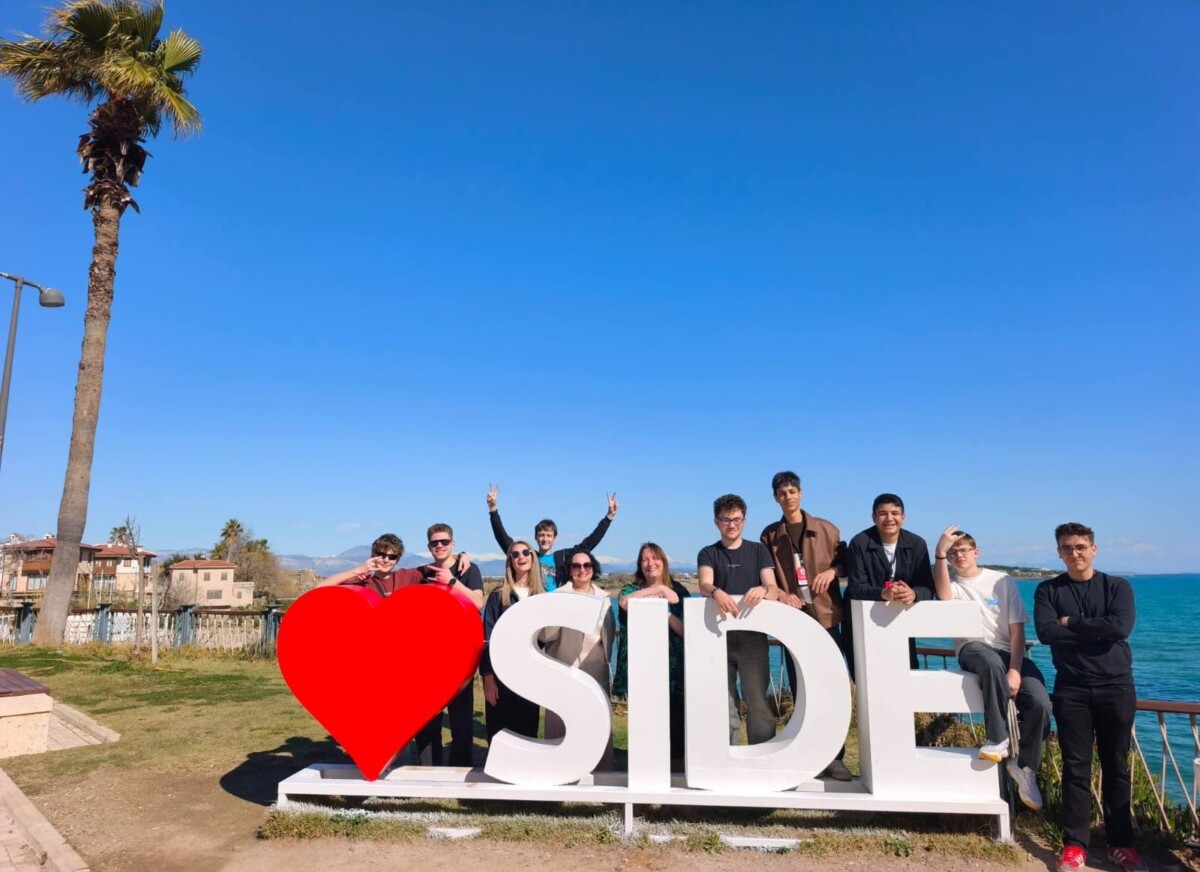 Jauniešu grupa pozē pie liela balta uzraksta, kas veido vārdu 