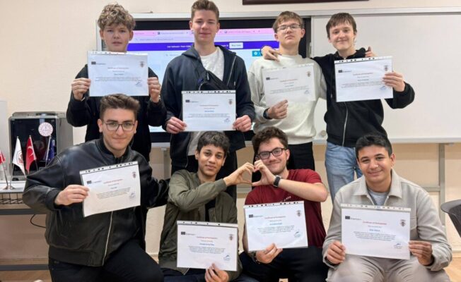 Astoņi jaunieši mācību telpā, daži stāvot, citi tupus, katrs tur rokas priekšā Erasmus+ 