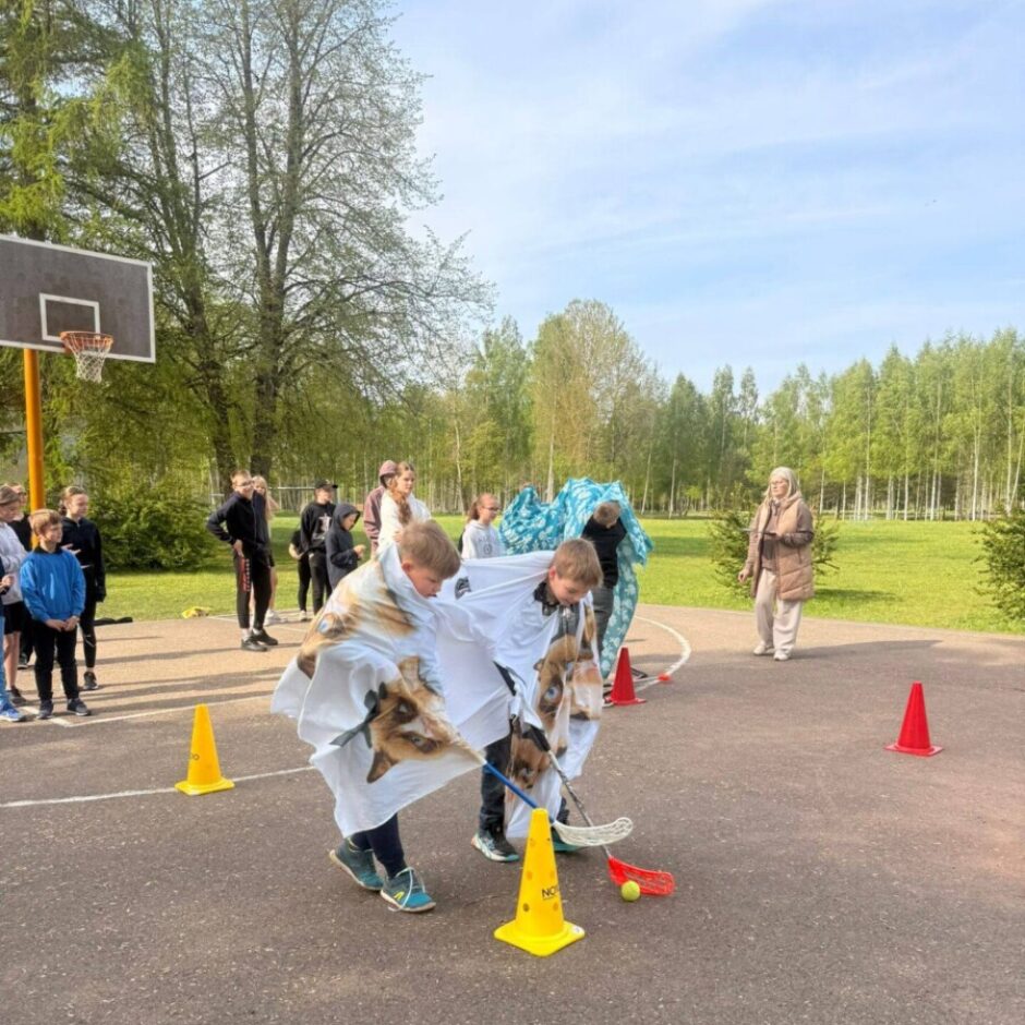 Ārā uz asfalta laukuma divi zēni, apsegti ar segām ar suņu sejām, spēlē florbolam līdzīgu spēli, virzot dzeltenu bumbu ar nūjām ap dzelteniem konusiem. Uz viena konusa redzams uzraksts 